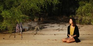 a woman sitting on the ground in front of a body of water