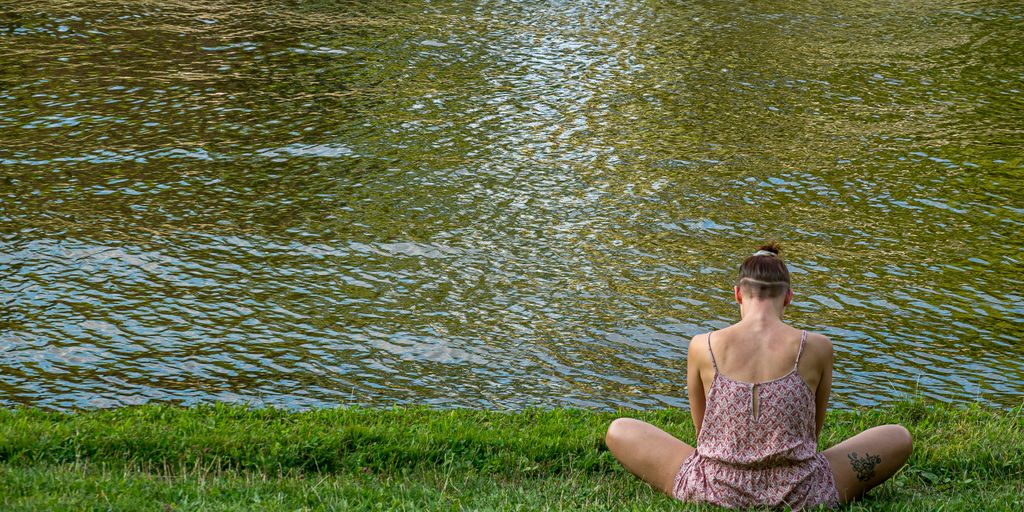 woman in brown tube dress sitting on green grass field near body of water during daytime